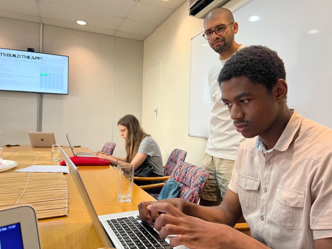 Barrett Flowers helping an attendee build an AI tool on his own laptop, with the build brief on screen behind them.